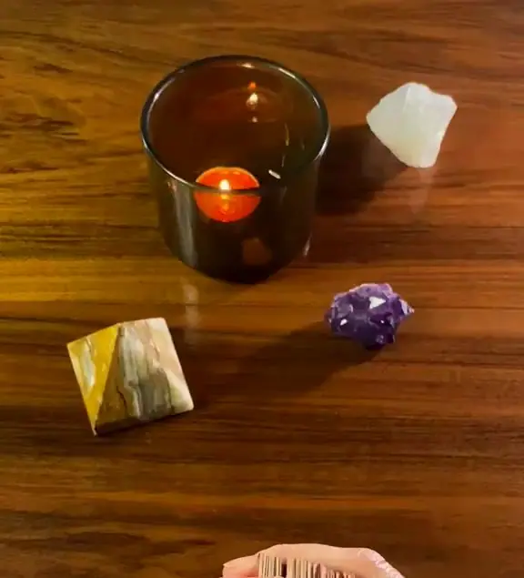 Brennende Kerze, Bergkristall, Amethyst und eine Steinpyramide auf einem Holztisch